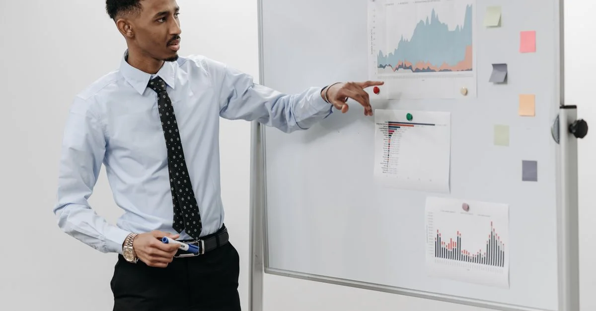 Homme présentant des données commerciales avec des graphiques sur un tableau blanc lors d'une réunion.
