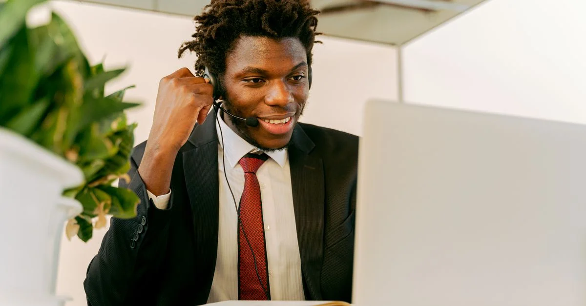 Homme d'affaires heureux avec des cheveux afros, portant un casque et un costume, travaillant sur un ordinateur portable dans un bureau.
