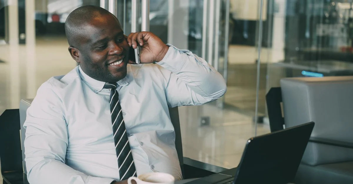 Homme d'affaires souriant parlant au téléphone tout en travaillant sur son ordinateur portable dans un bureau moderne.