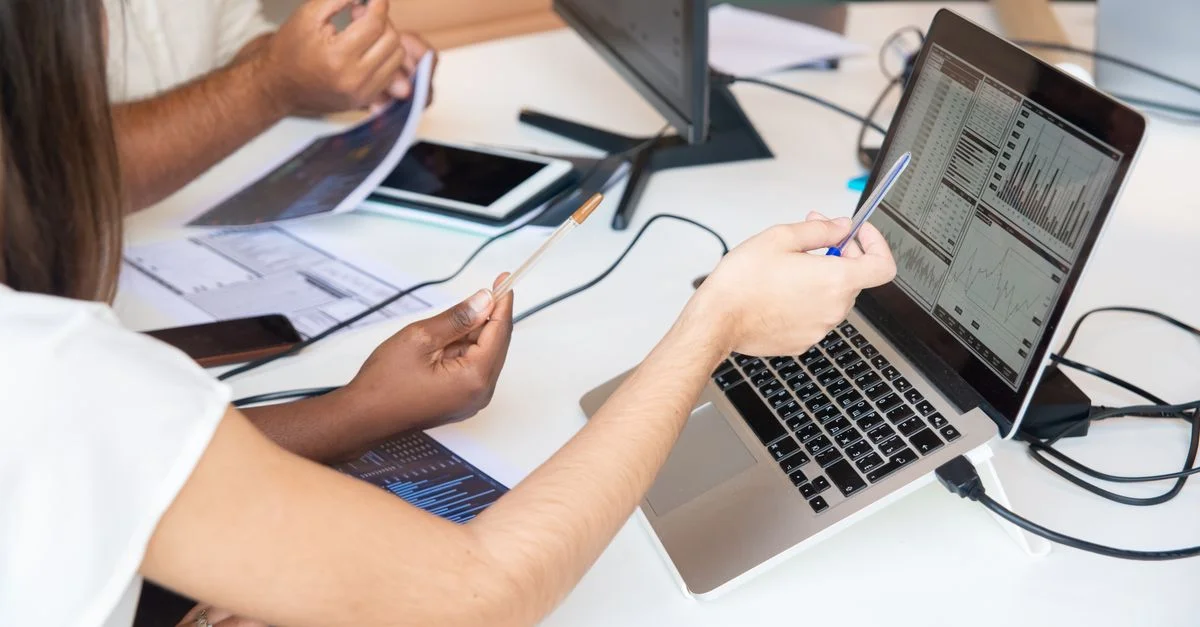 Des professionnels analysant des graphiques de données sur un ordinateur portable dans un environnement de bureau, discutant ensemble des insights.